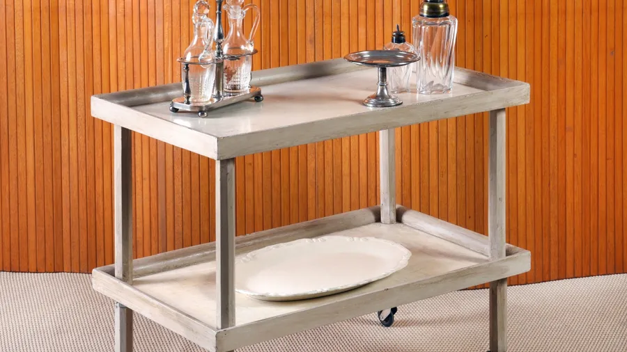 A stylish serving cart with glass bottles and silverware on a wooden background.
