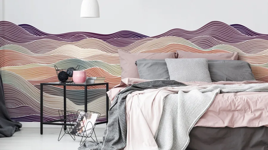 A modern bedroom with colorful mural walls, pink and gray bedding, and a tidy bedside table.