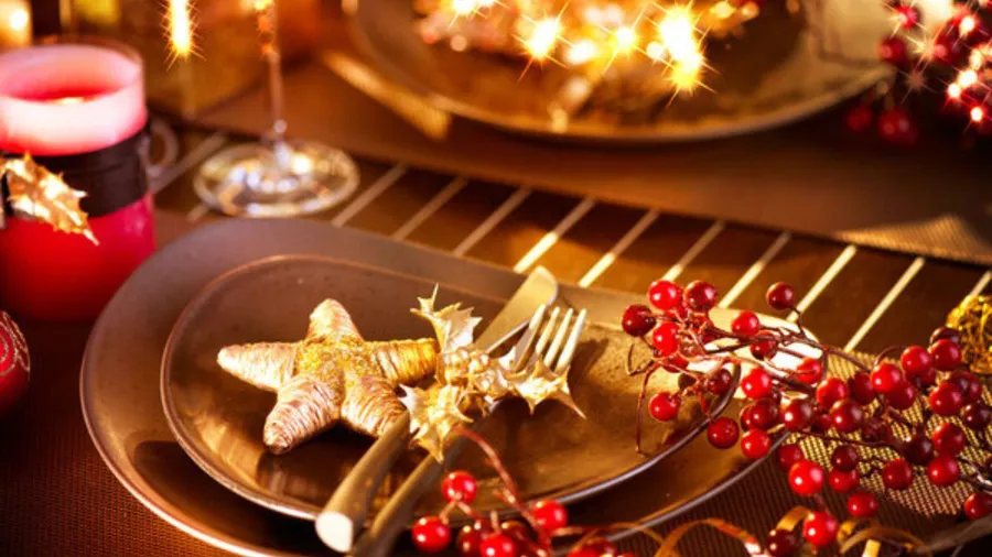 A festive dining table set for New Year Eve celebration, featuring a star-shaped decoration, cutlery, candles, and decorative berries.