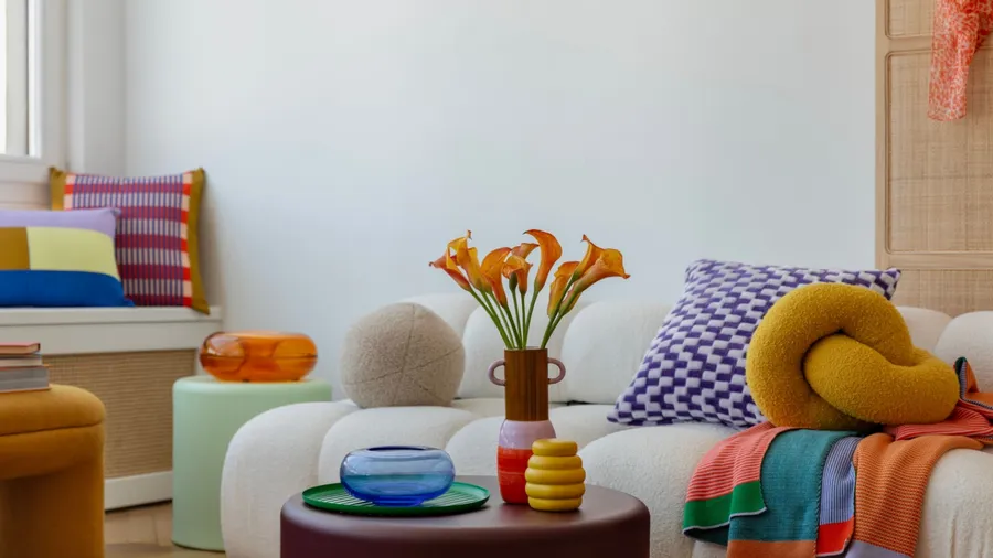 A colorful living room featuring a white curved sofa with bold, playful pillows