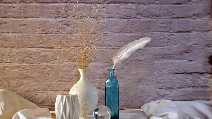 Elegant vases with dried plants and feathers on a neutral-toned surface.