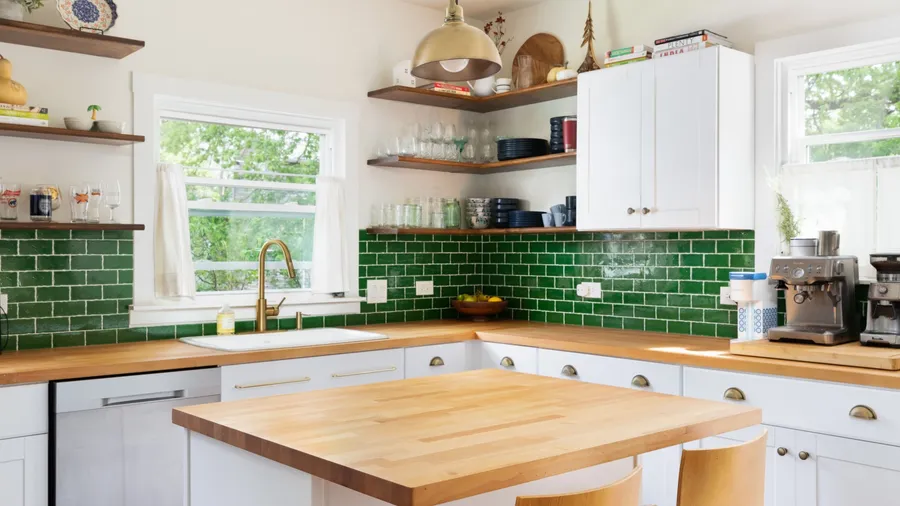 A sunny kitchen with wooden shelves, green tile backsplash, and a large window.