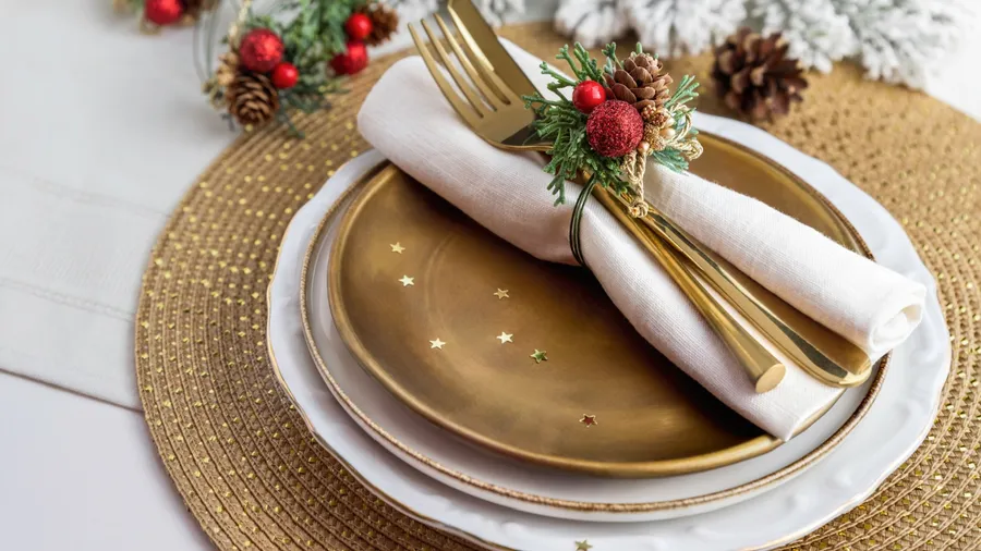 A holiday-themed place setting with gold dishes, a festive napkin, and Christmas ornaments.