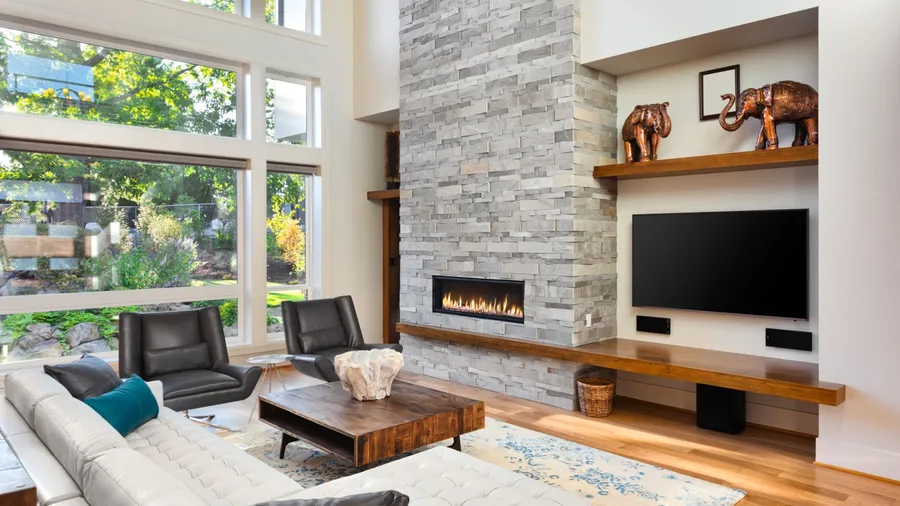 Modern living room with a stone wall, large windows, cozy sofa, leather armchairs, and wooden coffee table.