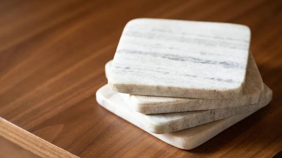 Four square marble coasters stacked on a wooden table.