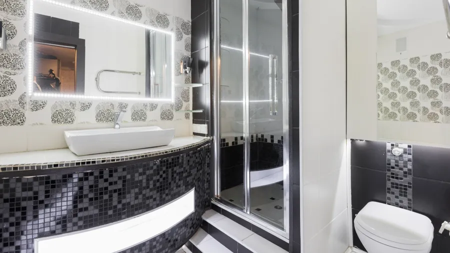 A bathroom interior with black glossy tiles, sink, mirror, and wall-mounted toilet.