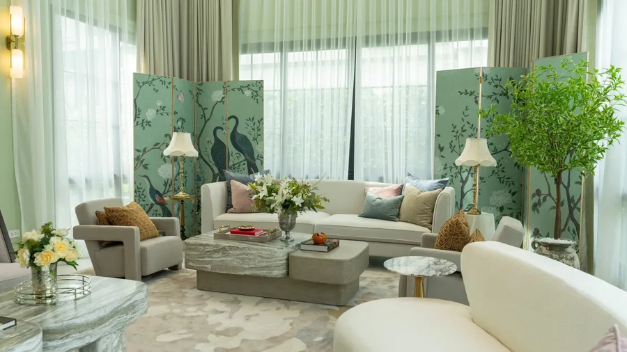 A well-decorated living room with a white sofa, armchairs, a coffee table, and a decorative screen featuring bird illustrations.