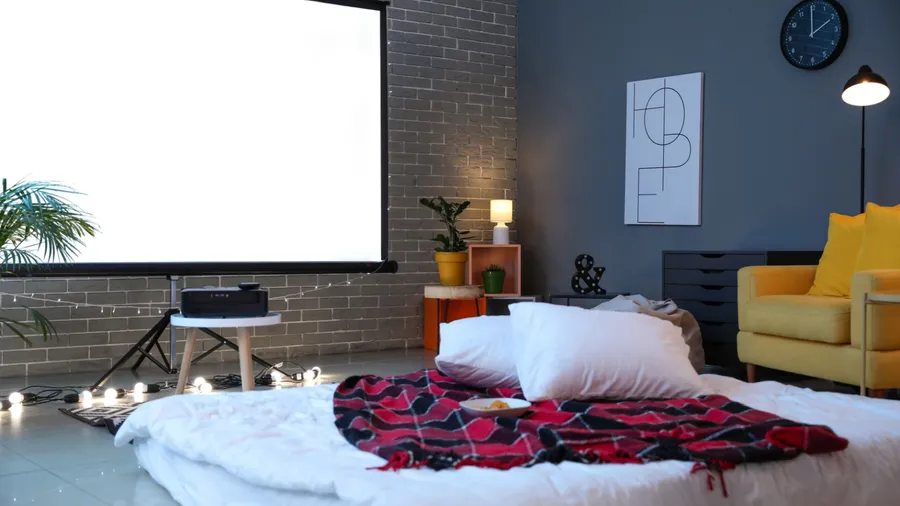 A modern living room with a large white projection screen, a yellow sofa, and a lamp.