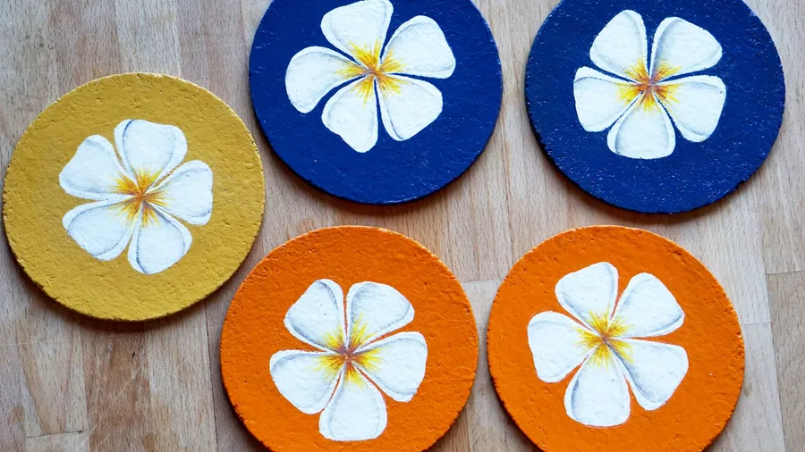 Cork coasters with flowers painted on them on a wooden table.
