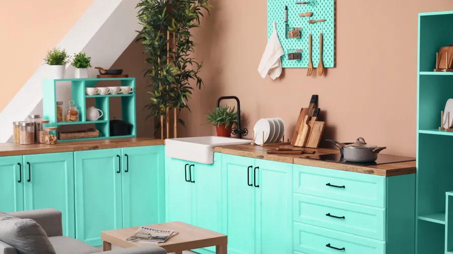 A kitchen interior with turquoise cabinets, wooden countertop, plants, shelves, and a pegboard on a beige wall.