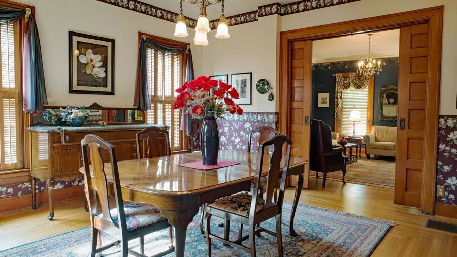 Elegant Victorian dining room with patterned wallpaper, soaring high ceilings, and a silver chandelier as the centerpiece.
