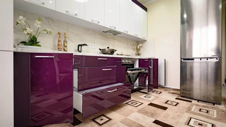 A kitchen interior with purple drawers, white and purple cabinets, refrigerator, and a marble countertop.