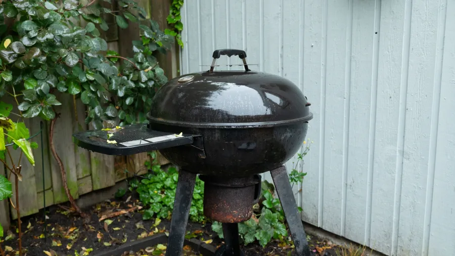 An old kettle grill stands in a backyard, showing signs of weathering