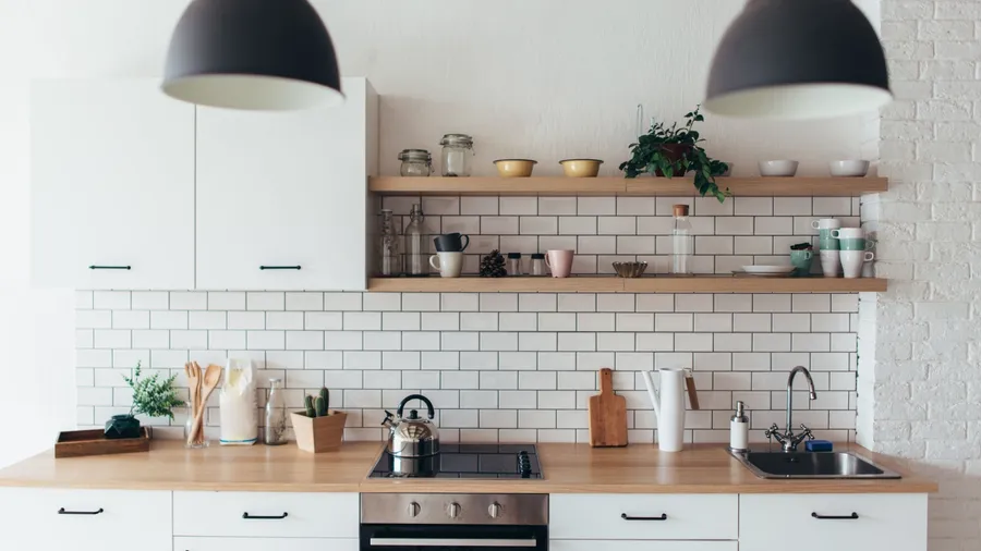 A kitchen interior with white cabinetry, butchers block countertop, pendant lights, and open shelving displaying mugs, jars, and dinnerware.