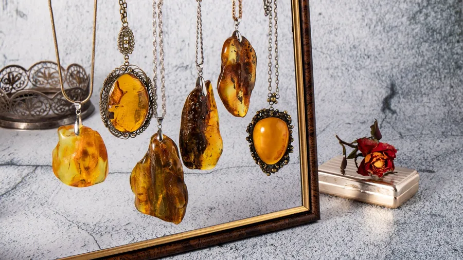 Amber-colored gemstone necklaces hanging in a frame; some flowers and decorative items nearby.