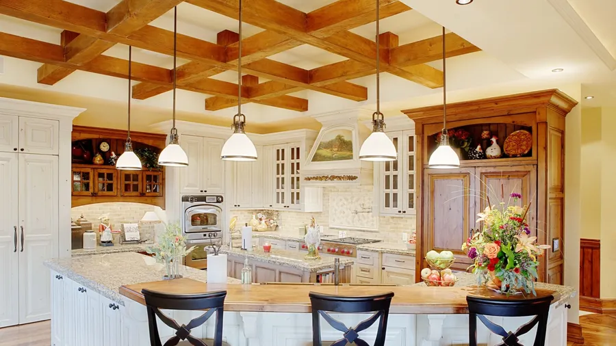 A beautiful kitchen interior with exposed wood beams ceiling, pendant lights, marble countertop, and white cabinetry.