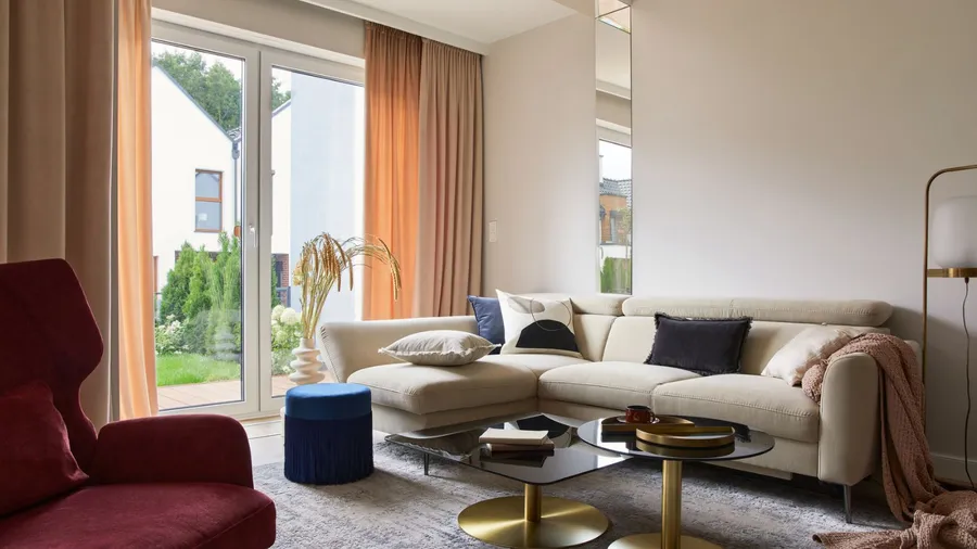 A modern living area featuring a beige sectional sofa, large windows, coffee table, rug, ottoman, and vibrant curtains.