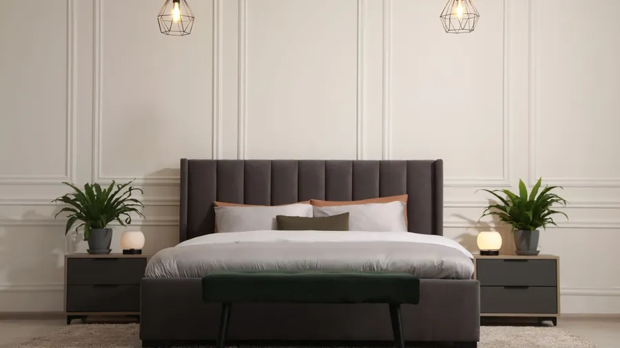 A minimalistic bedroom interior with a cozy bed, bench, rug, nightstands with lamp and plants, and pendant lights hanging from the ceiling.