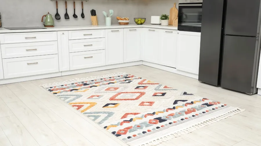A bright kitchen with white cabinets and a colorful geometric rug on the floor.