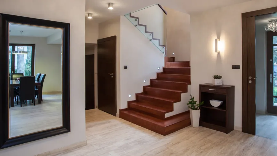Travertine house: hallway A modern hallway with wooden stairs, a glass railing, and a large mirror.