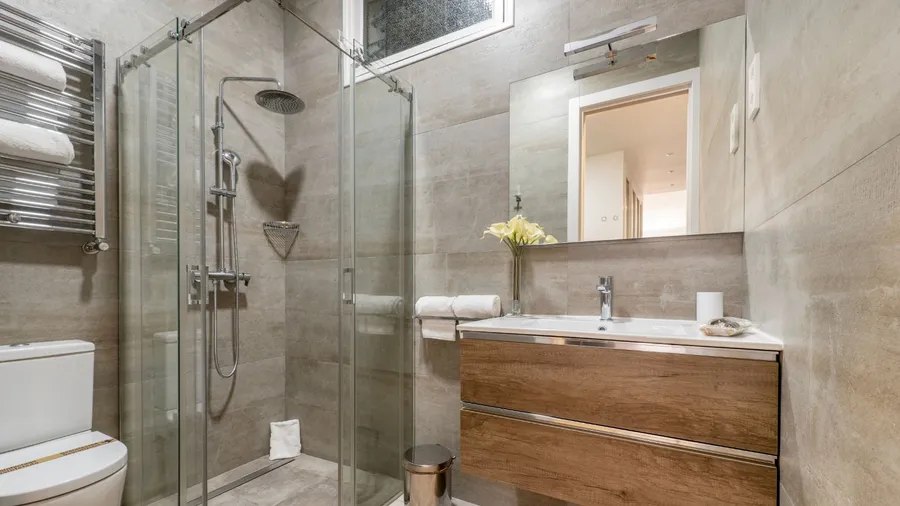 A stylish bathroom interior with marble tiles, wooden drawers, frameless glass shower, and a mirror on the wall.