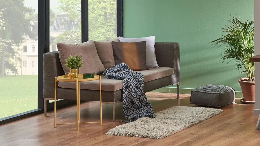 A stylish living room with a cozy sofa, throw blanket, cushions, coffee table, floor cushion, and a rug on a wooden floor.