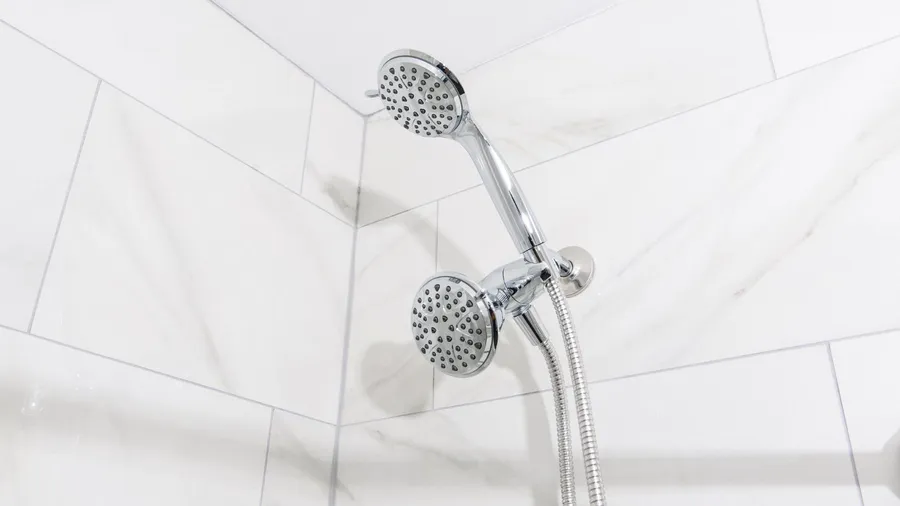 A modern chrome dual showerhead system with adjustable handheld spray mounted on the marble tiles wall.