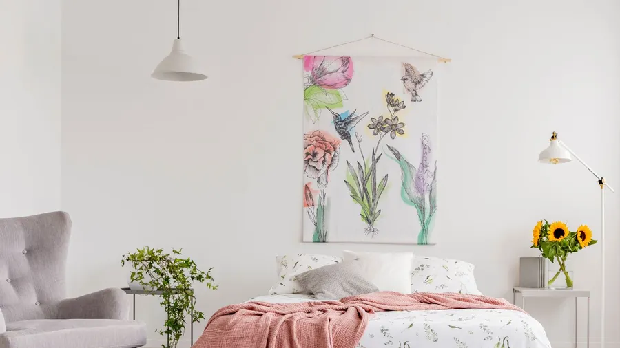 Nature lover's bright bedroom interior with a wall art of flowers and birds painted on a fabric above a bed which is dressed in green plants pattern on white linen. Real photo.