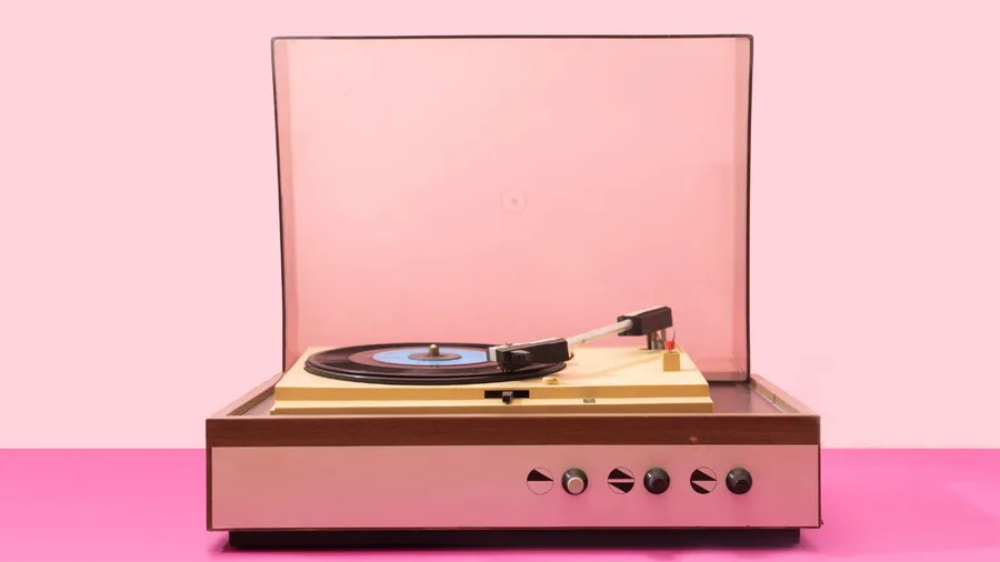 A pink retro vinyl record player on a pink surface in front of a light pink wall.