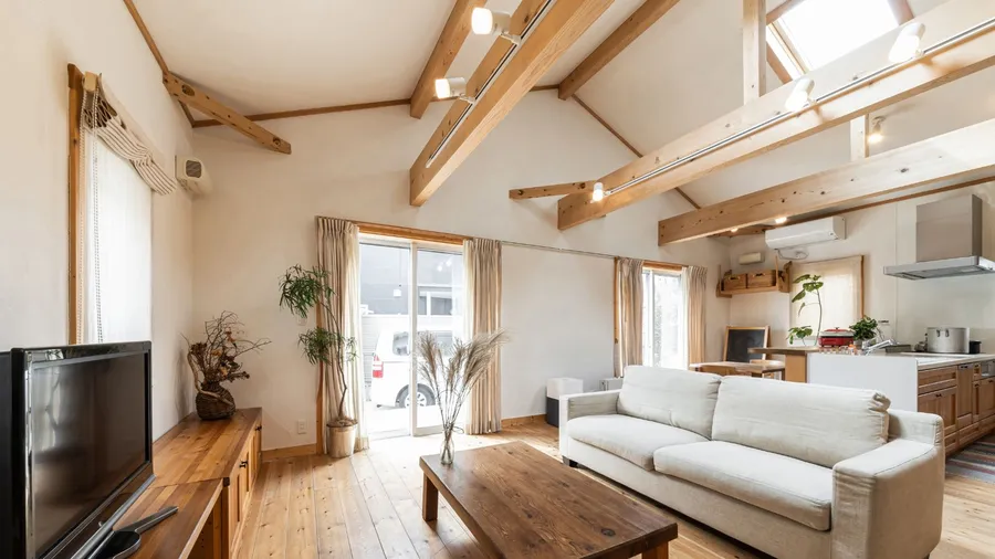 A living room interior with wooden coffee table, sofa, exposed wood beam ceiling, and potted plants.