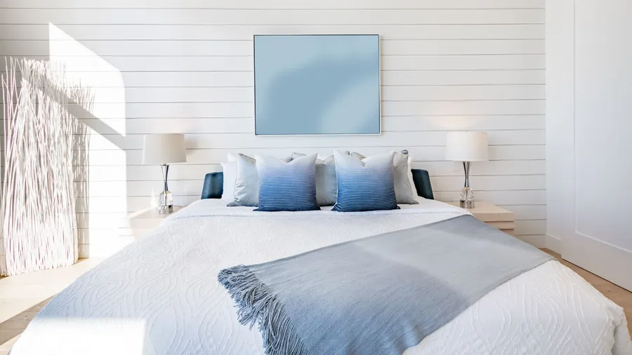 A stylish bedroom with a cozy bed, throw blanket, pillows, bedside tables, lamps, and a poster on a shiplap wall.