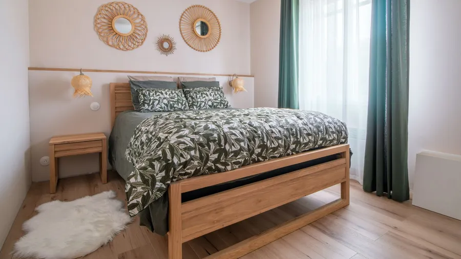 A bedroom interior with wooden bed, woven wall hangings, wooden side table, and a white wool rug on the floor,