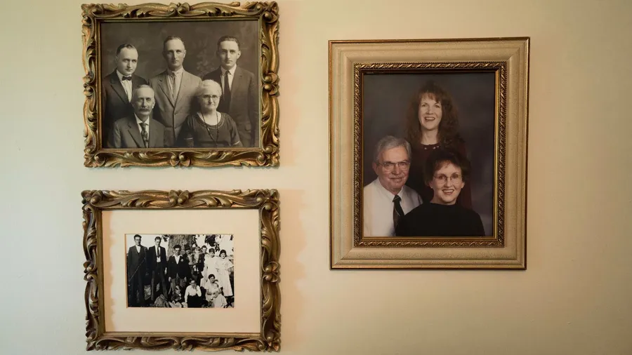 Vintage picture frames with old family photographs hanging on a beige wall.
