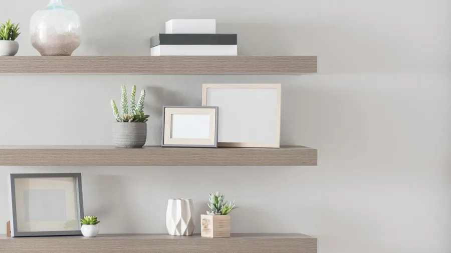 Wooden floating shelves on a neutral wall with frames, small potted plants, and decor accents.