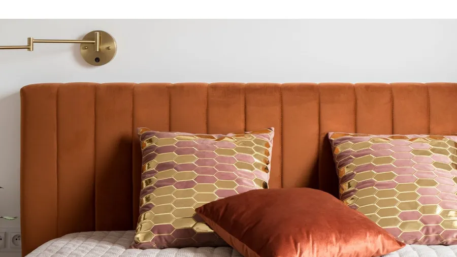 A velvet upholstered headboard on a cozy bed with velvet throw pillows on it.