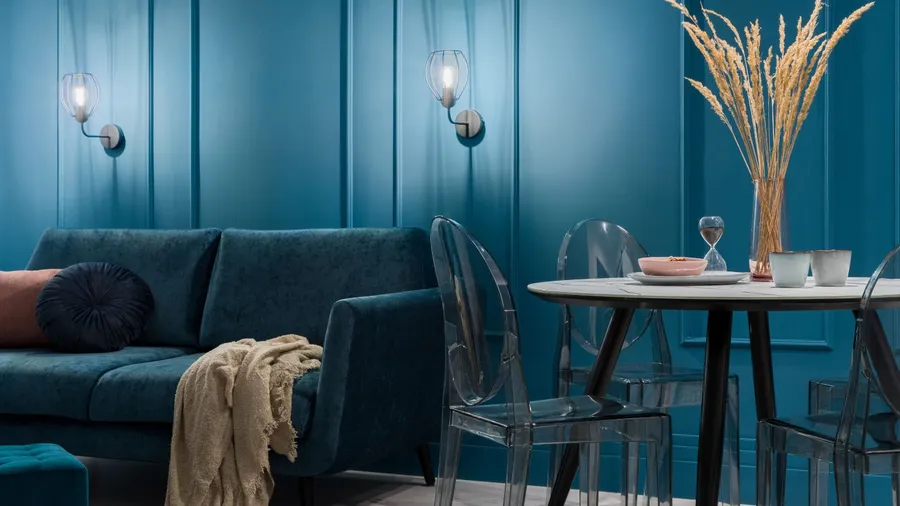 A vibrant blue space featuring a plush sofa, glass dining table, and decorative grasses.