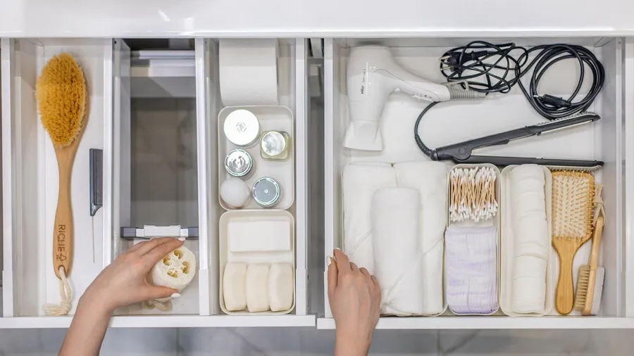 A woman organizing bathroom toiletries and amenities in a drawer organizer.