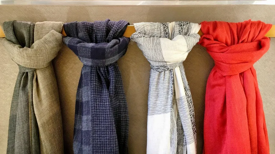 Different vintage scarves hanging from a wooden rod.