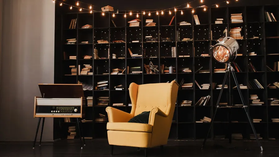 A cozy reading corner with a vibrant yellow armchair next to a vintage record player and a bookshelf, softly lit by string lights.