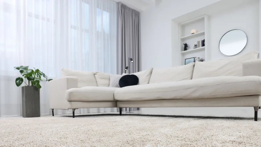 A living room interior with white sofa, rug, mirror, and layered sheer curtains on big windows.