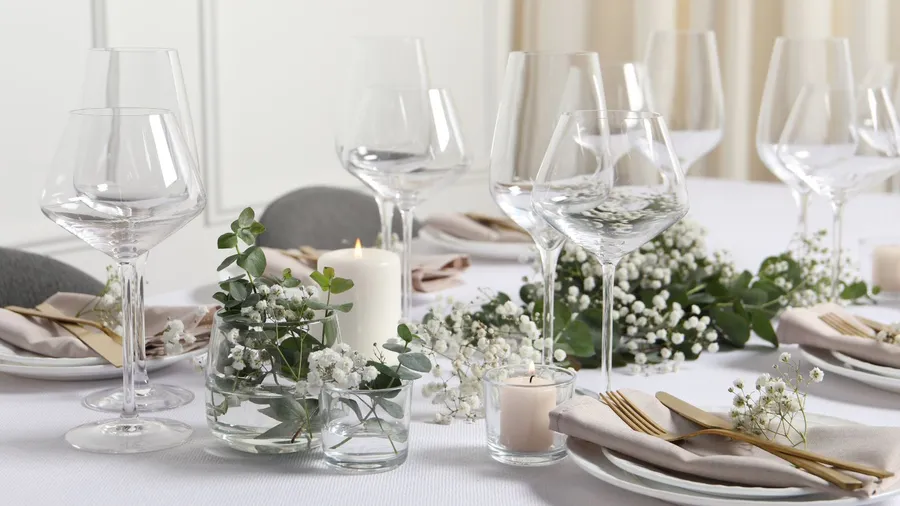 A beautiful table setting with dinnerware and candles and eucalyptus leaves and flowers.