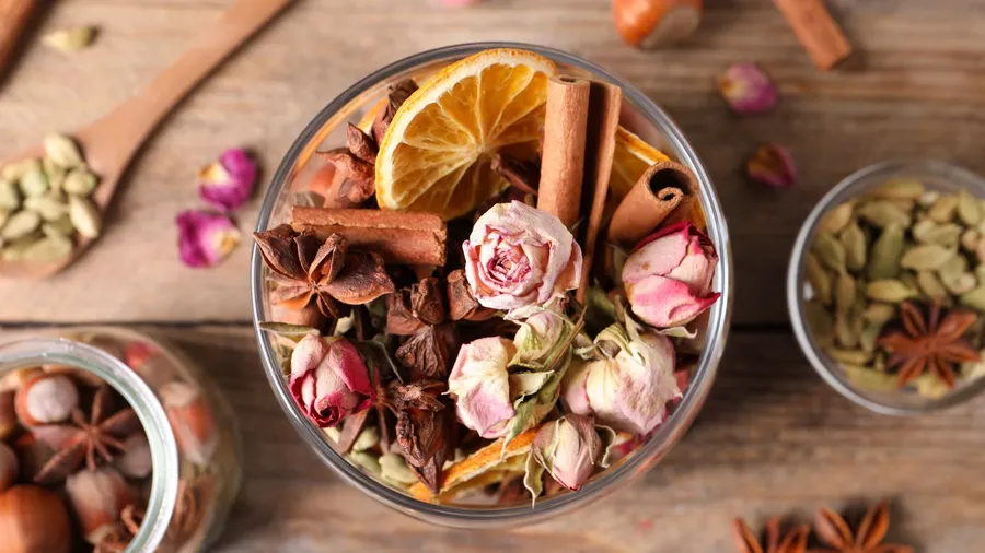 A close-up of dried flowers, spices, and herbs in glasses on a wooden surface.