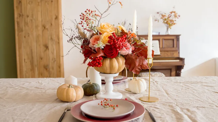 A thanksgiving table decor with flower bouquet in a pumpkin, candles, and dinnerware.