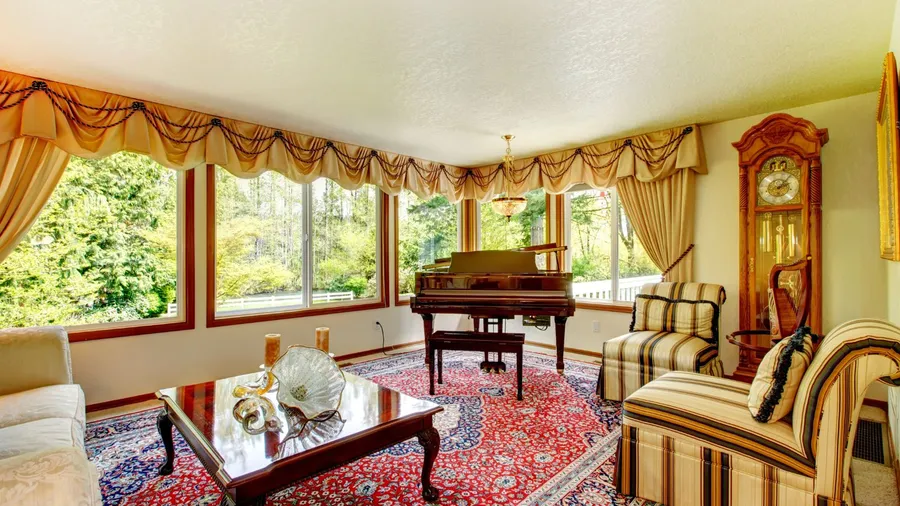 A vintage living room interior with sofa, wooden coffee table, piano, curtains, grandfather's clock, and Persian rug.