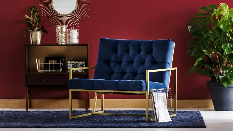 A navy blue velvet armchair with golden frame in front of a burgundy wall.