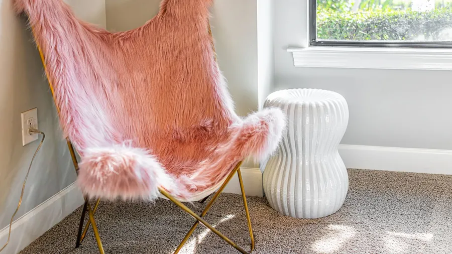 A pink faux fur cover on a metal chair and white coffee table near a window.