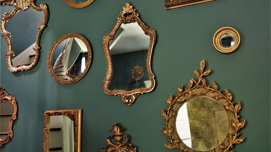 Vintage mirrors of different shapes and sizes with metallic frames hanging on a green wall.