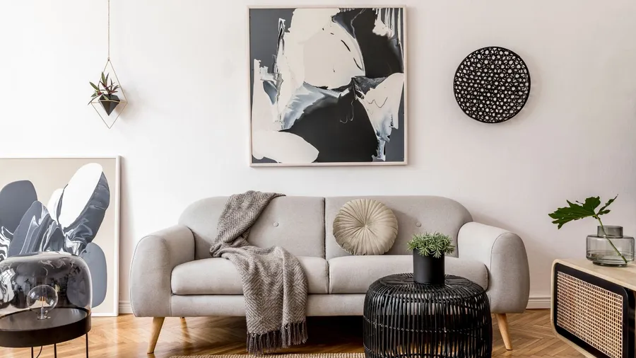 Stylish living room interior with gray sofa, pillows, plaid, plants, and abstract paintings on the wall