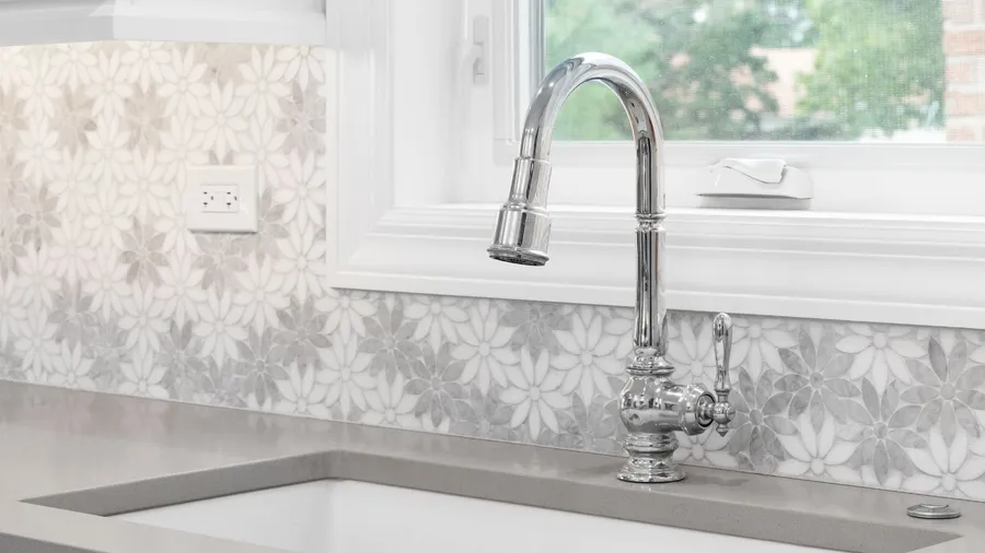 A chrome faucet in the kitchen with daisy flower stenciled backsplash.
