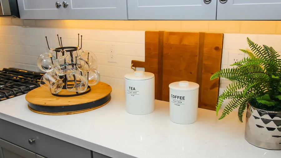 A kitchen counter with a mug holder, labeled jars for tea and coffee, and a green plant.